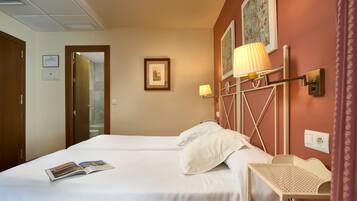 Habitación de hotel con dos camas, una mesita y una lámpara.