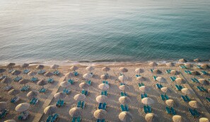 An aerial view of a beach with rows of blue lounge chairs and straw umbrellas. - Mitsis Rodos Maris (Rhodes)
