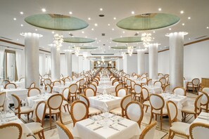 Une salle de banquet avec des tables et des chaises rondes, de grandes colonnes et des lustres.