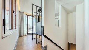 Un interior moderno con suelo de madera, una escalera con barandilla metálica y vistas a un balcón exterior con cortinas.