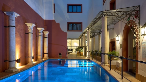 Un área de piscina con columnas, un paseo techado y la entrada a un edificio.
