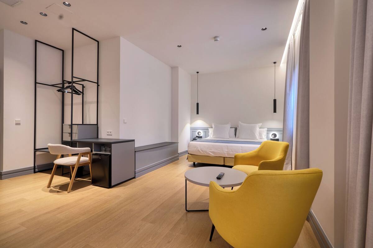 Una habitación de hotel moderna con cama, mesitas de noche, escritorio, silla y mesa redonda.
