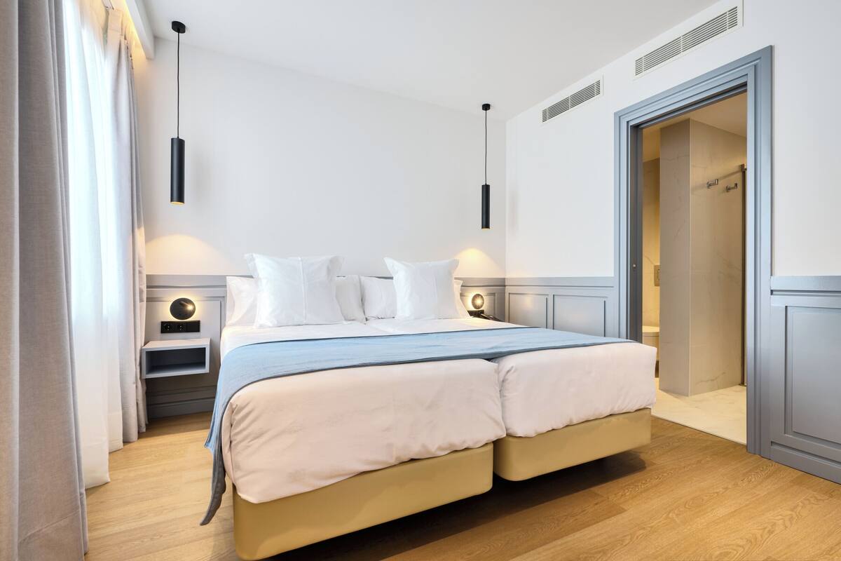 Una cama doble con cubrecama azul claro y color beige, mesitas de noche con lámparas y un armario con espejo.