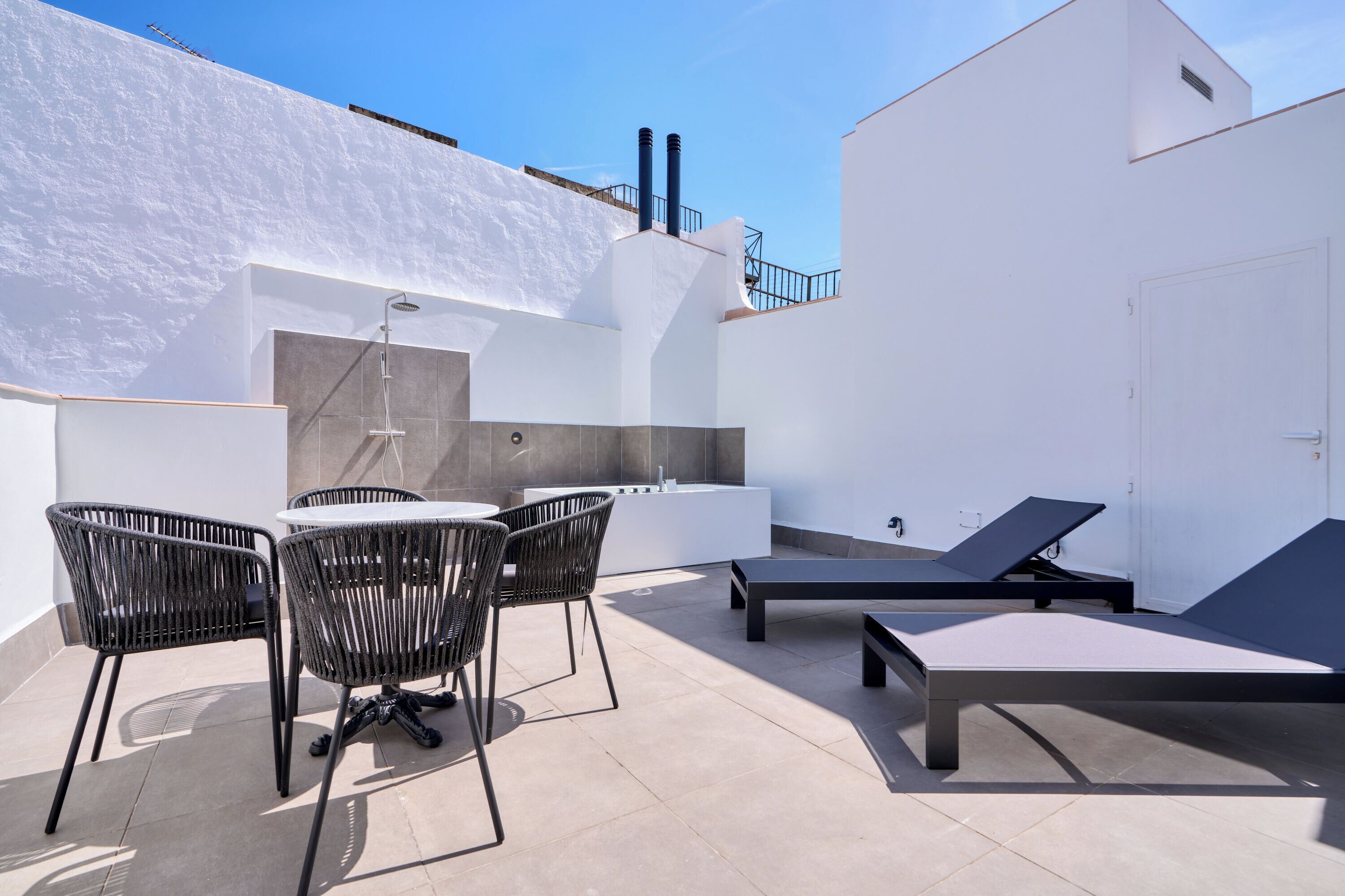 Una terraza en la azotea con mesa y sillas, un sillón de descanso y una pequeña cocina al aire libre.