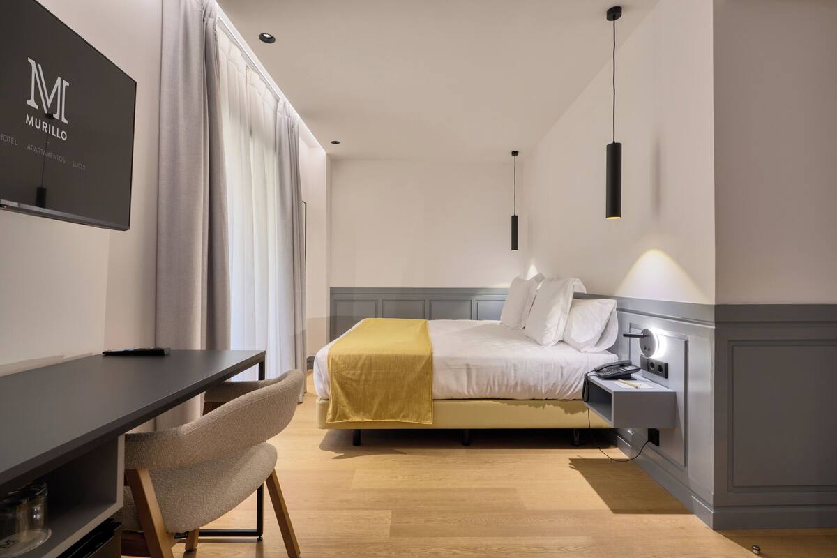 Una habitación de hotel moderna con una cama, mesita de noche, lámpara y televisión en la pared.