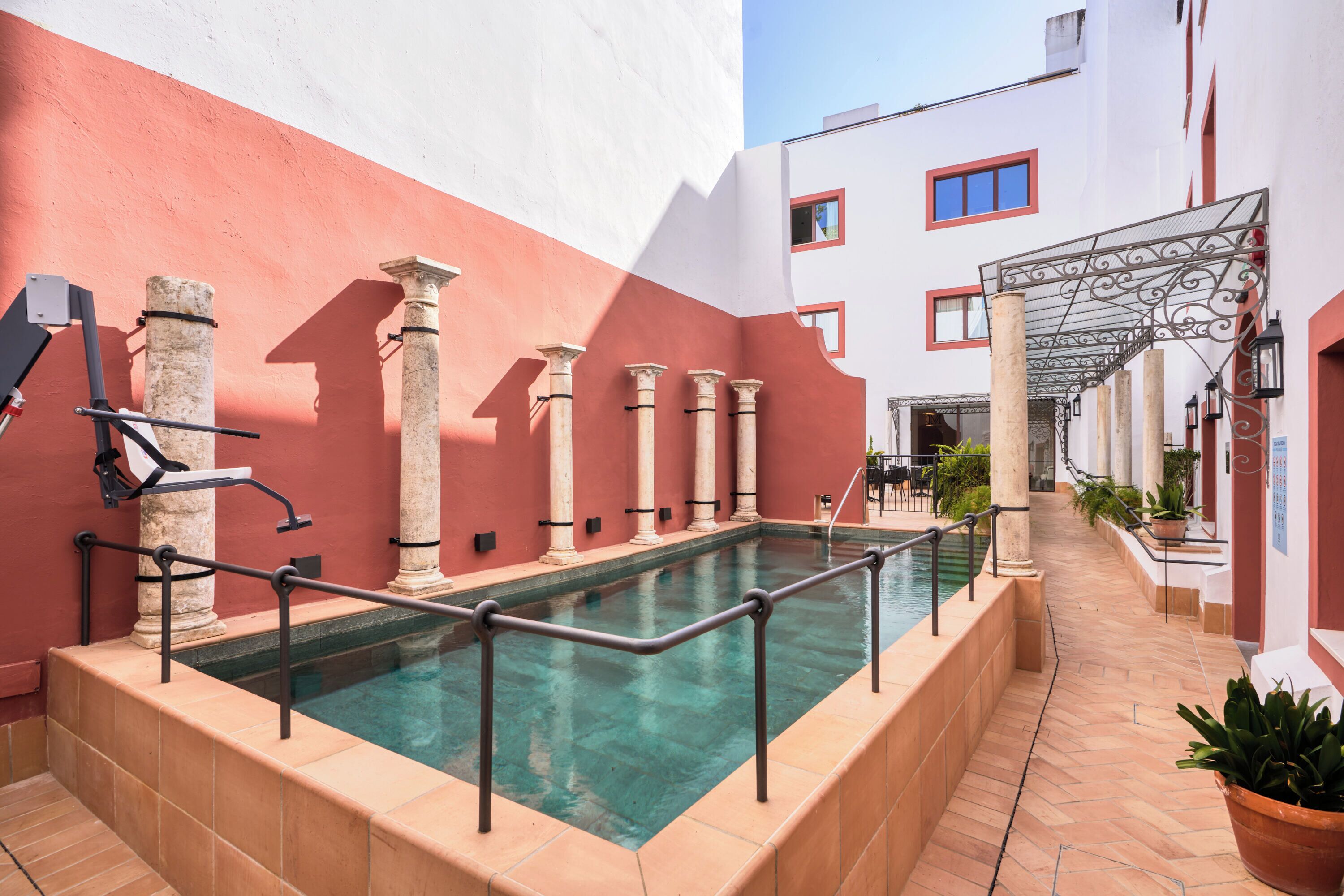 A pool area with a tiled deck, columns, and a covered seating area.