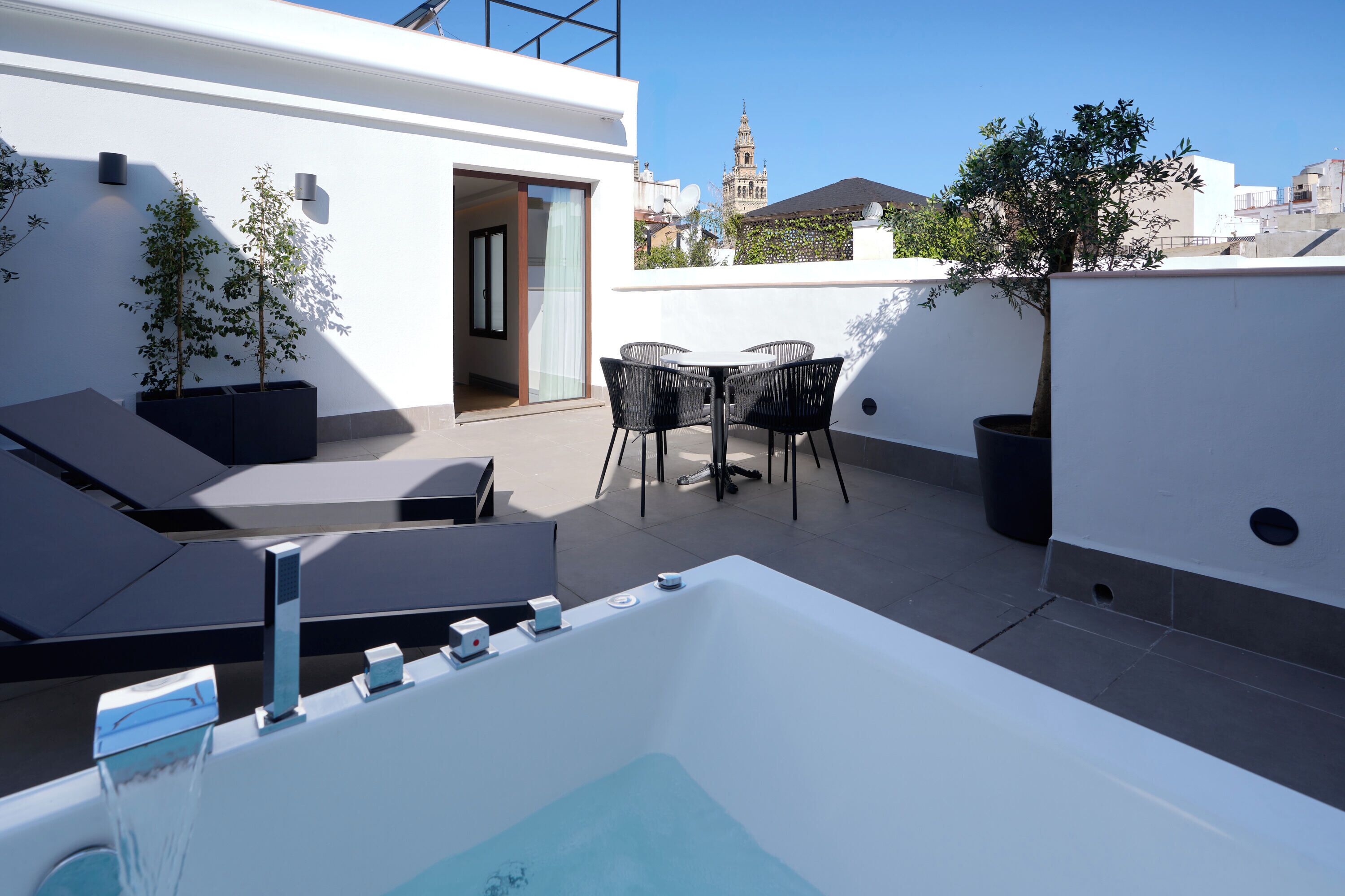 A rooftop terrace with a hot tub, lounge chairs, and a table with chairs.