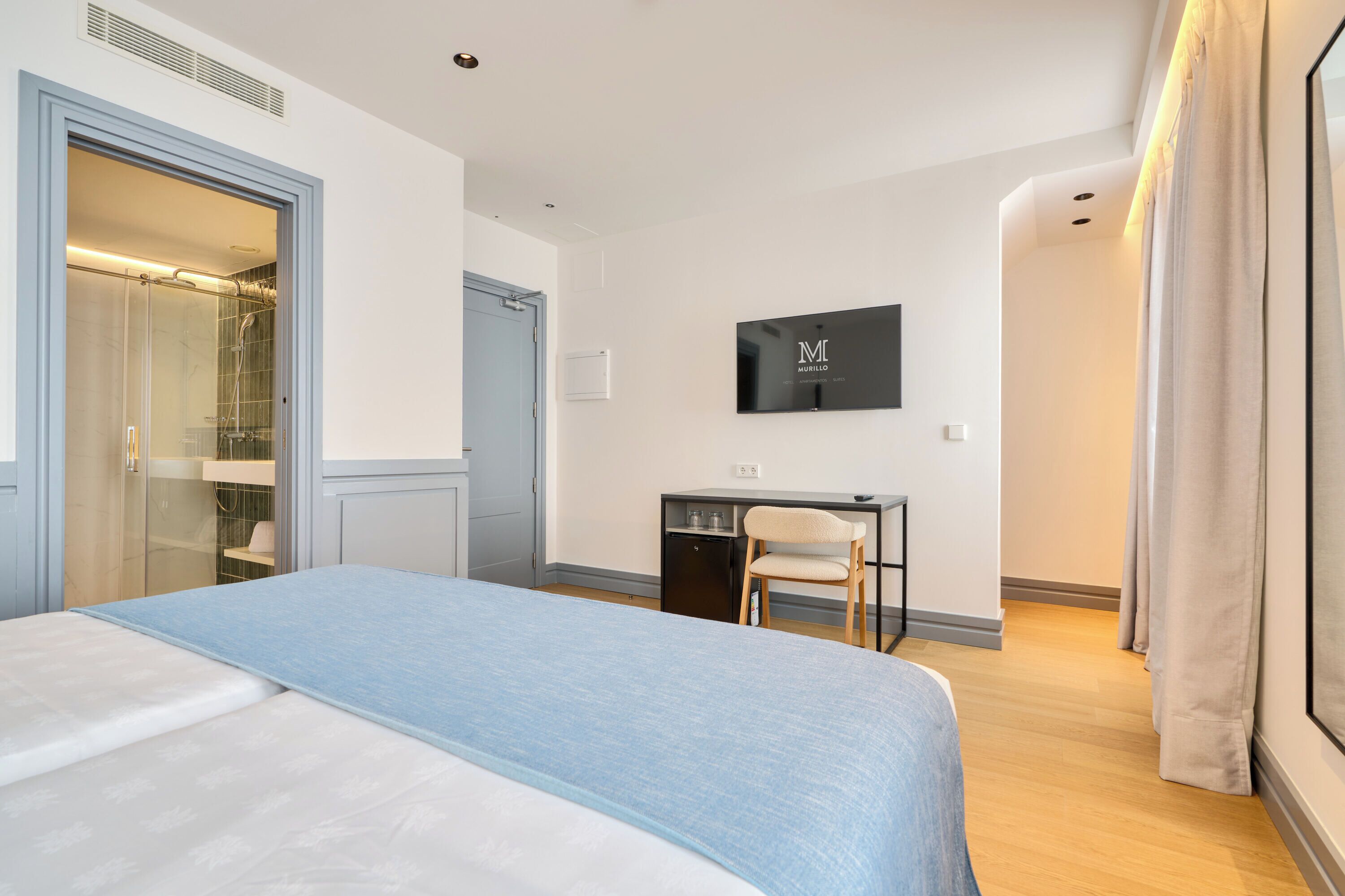 A hotel room with a bed, a desk, a chair, a TV, and a wardrobe.