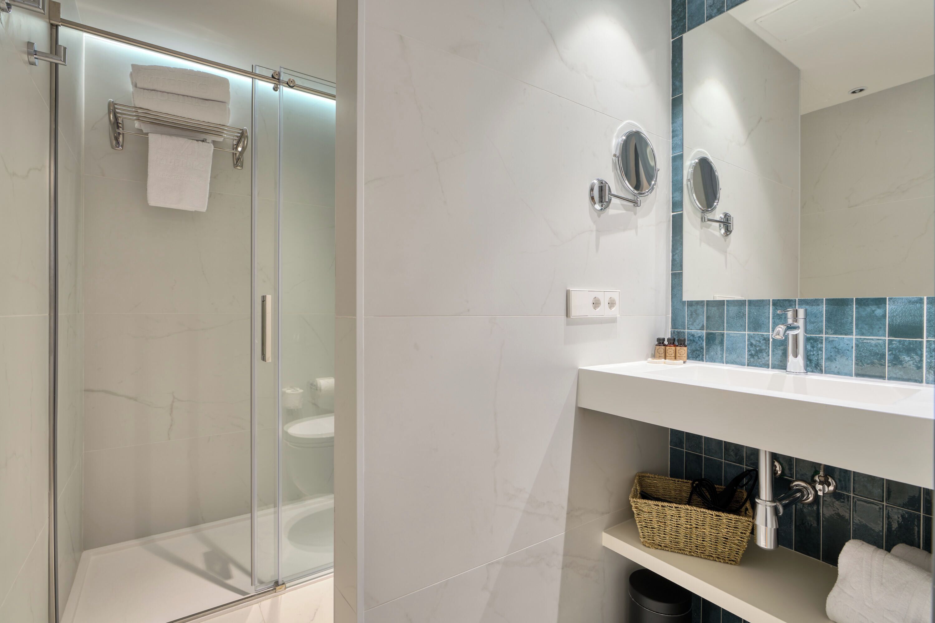 Un baño moderno con ducha envuelta en vidrio, un lavabo blanco con espejo y un salpicadero de azulejos.