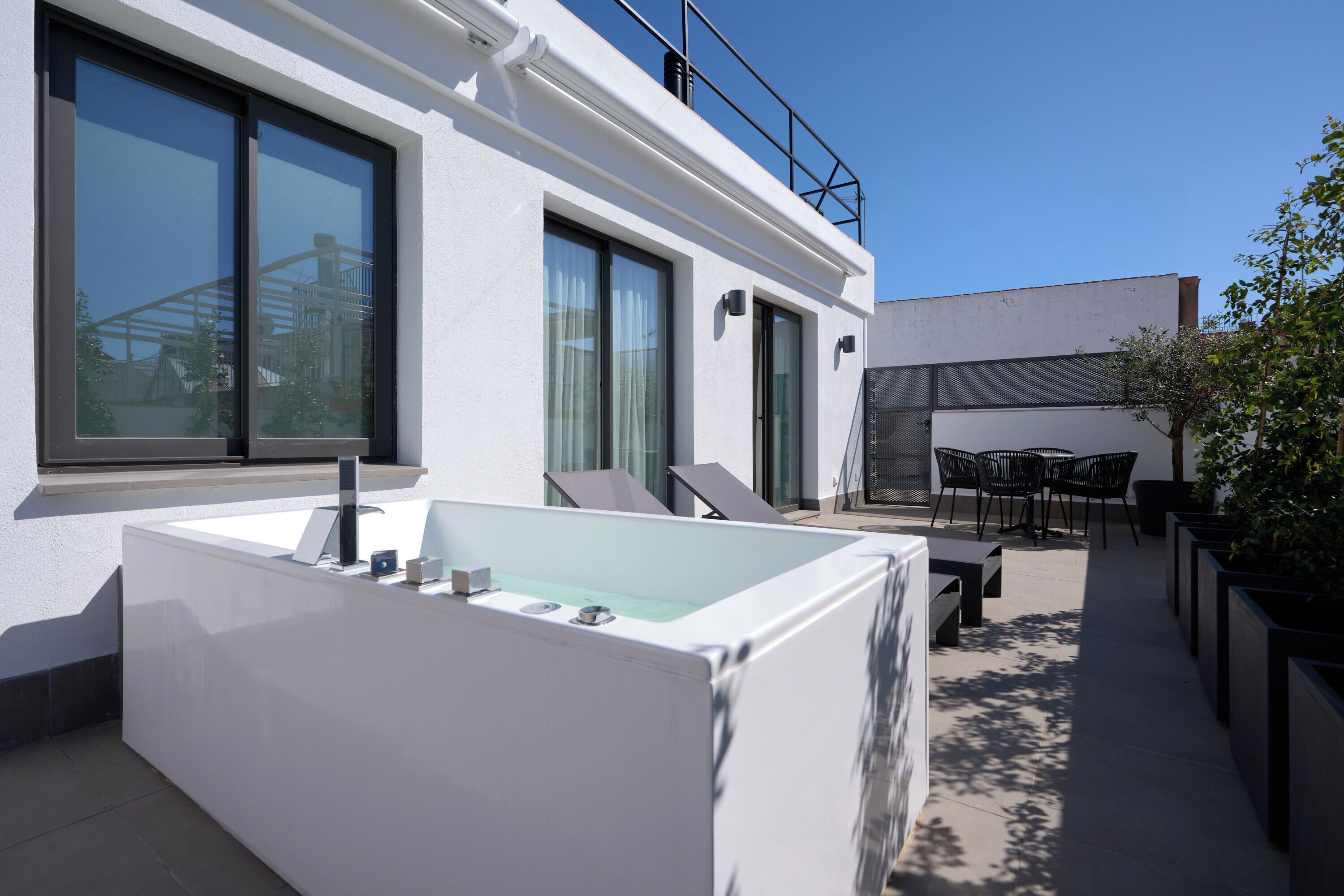 Un espacio exterior moderno con un amplio jacuzzi rectangular, una zona de estar con sillas y una vista despejada del cielo.