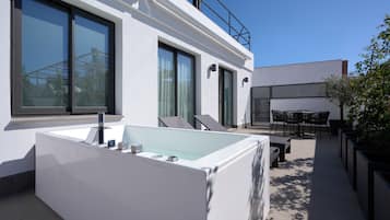 Un espacio exterior moderno con un amplio jacuzzi rectangular, una zona de estar con sillas y una vista despejada del cielo.