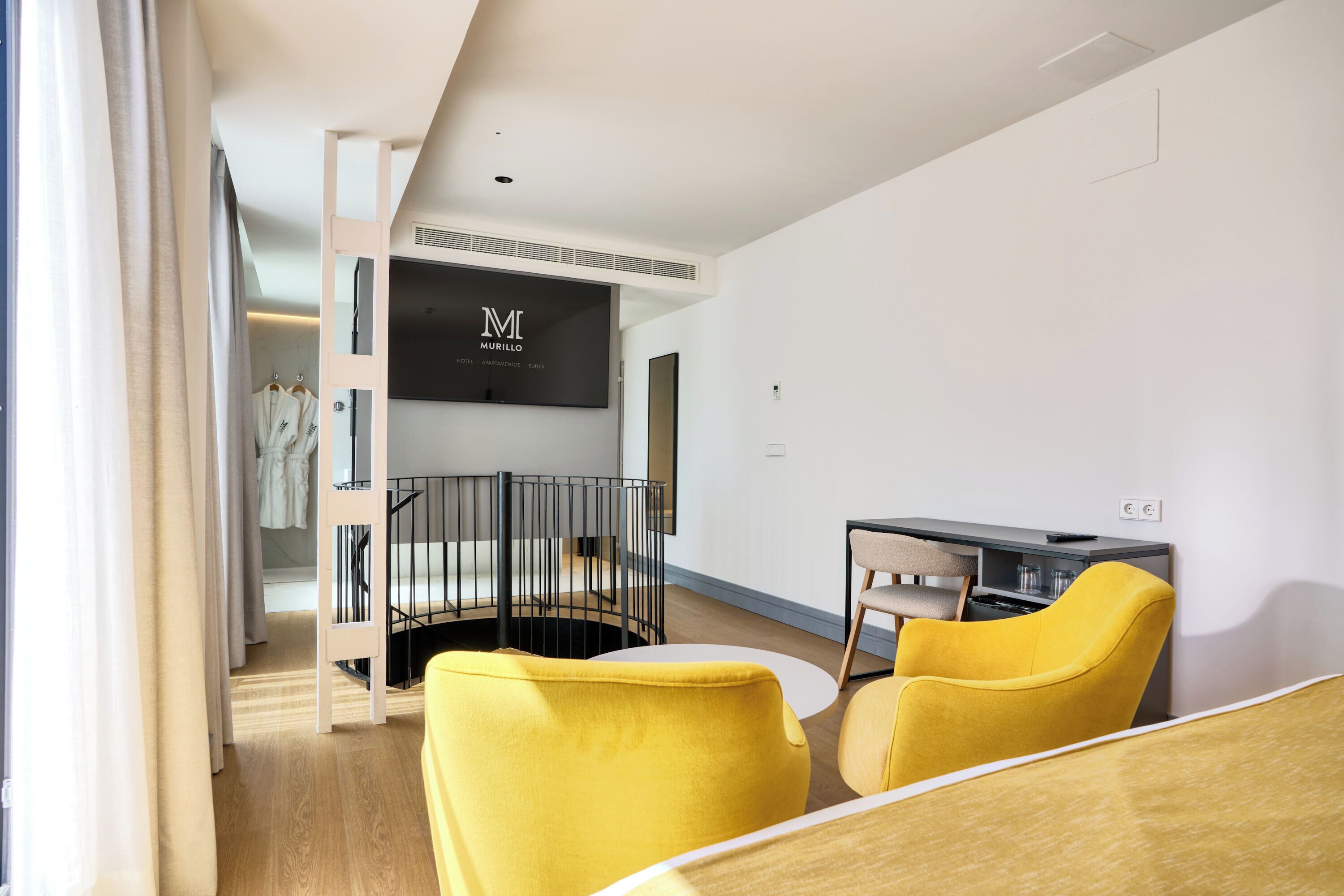 Habitació d'hotel moderna amb literes, escriptori i cadires grogues.