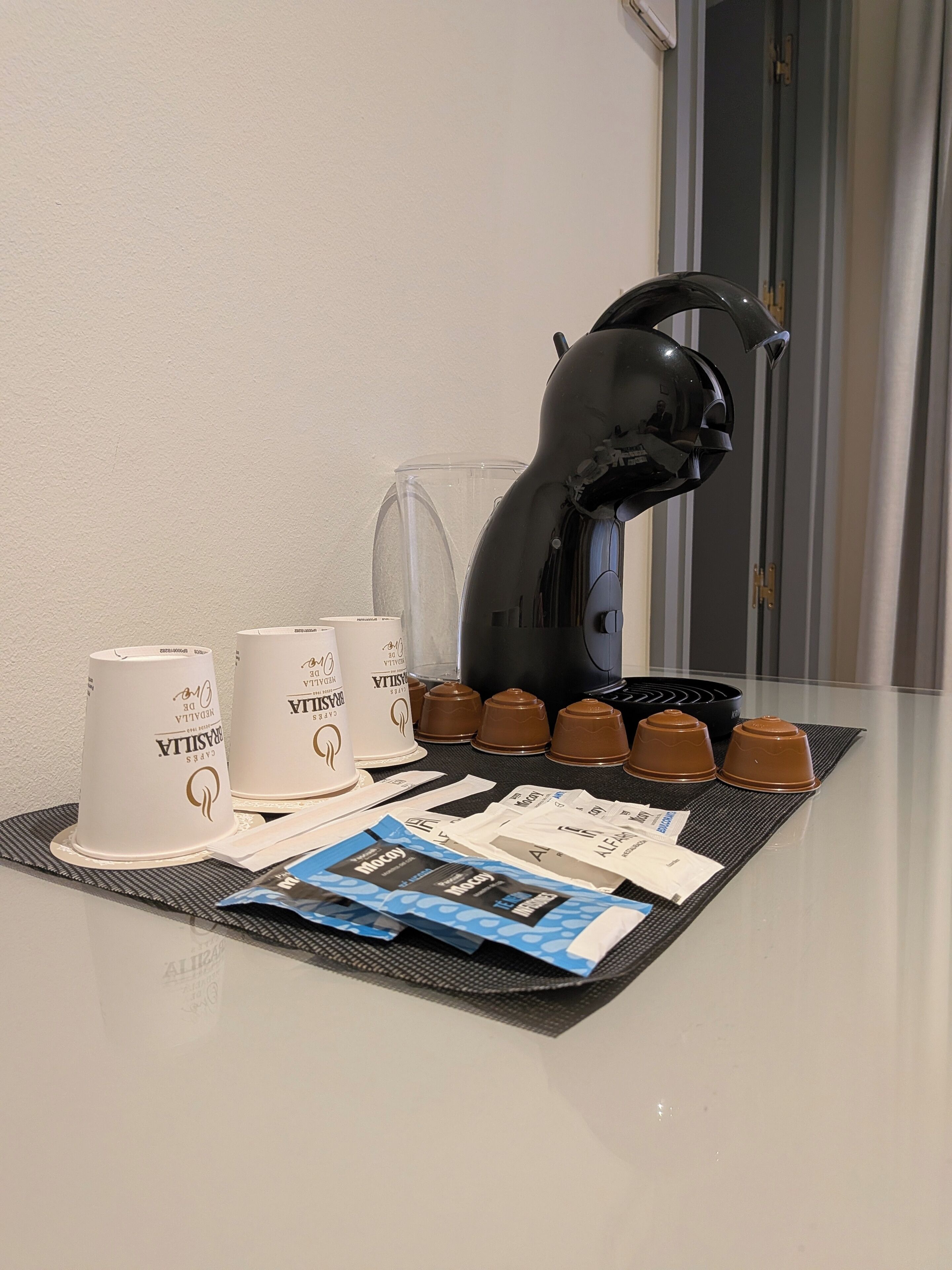 A coffee machine, two white cups, and several brown cups on a table with a placemat.