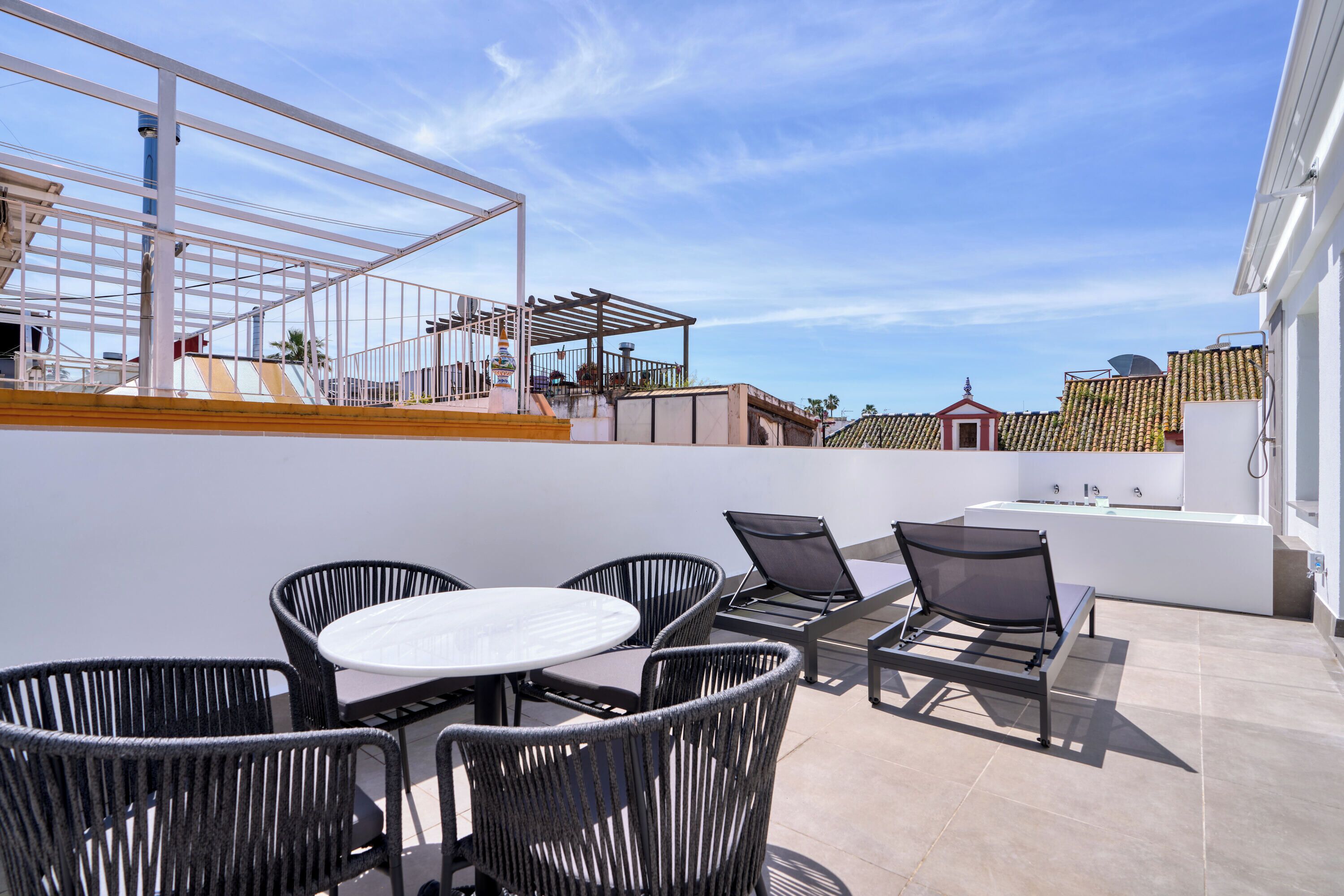 A rooftop terrace with a white table and chairs, a sun lounger, and a white bathtub.