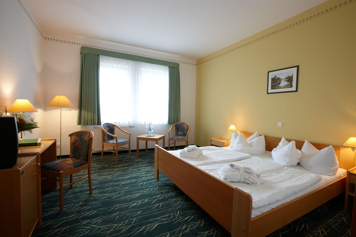 A hotel room with a bed, two chairs, a desk, a lamp, and a picture on the wall.