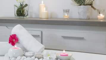 Een wellness omgeving met kaarsen, een bloem en een dienblad vol witte kiezelstenen.