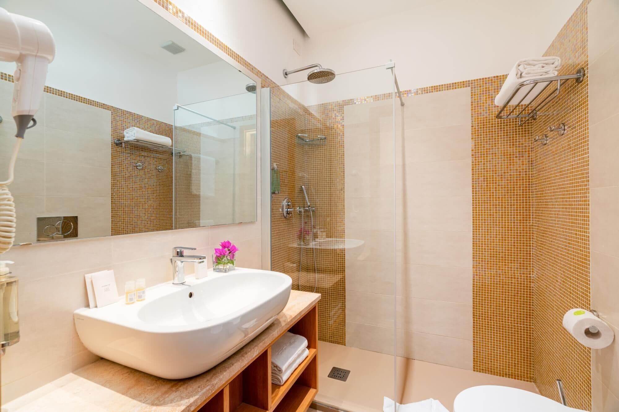 Un bagno moderno con un lavandino bianco grande, un box doccia in vetro e uno specchio sopra il lavandino.