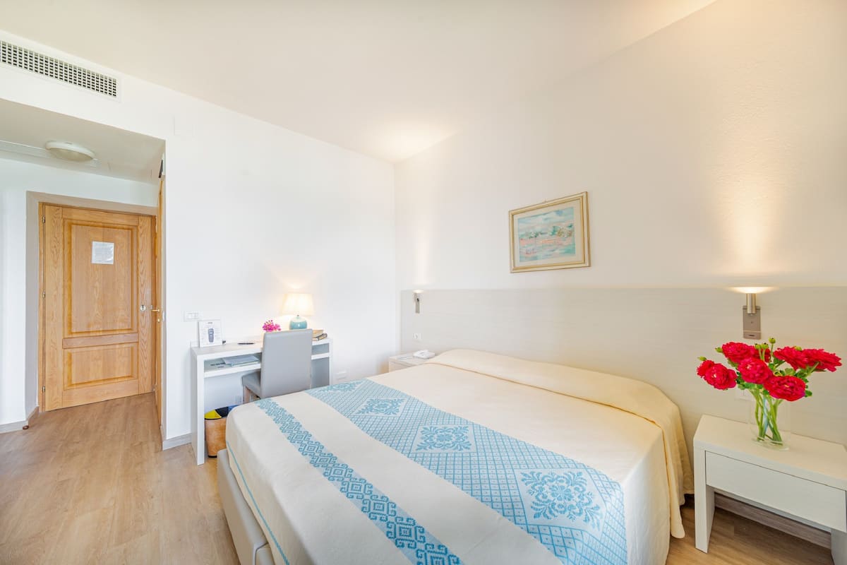 Ein Schlafzimmer mit Bett, Schreibtisch, Stuhl und Nachttisch mit Blumen.