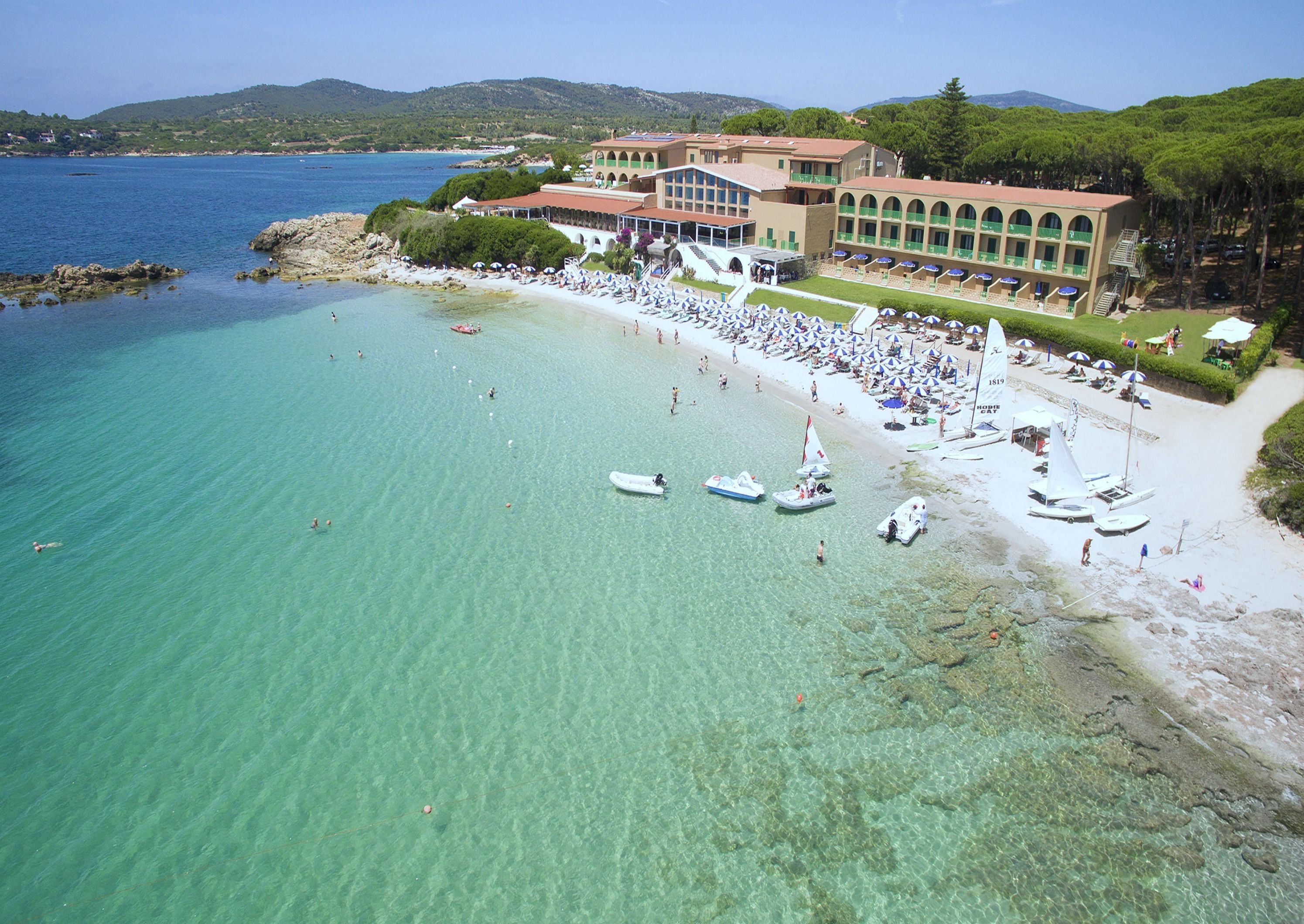 Un resort frente al mar, con aguas turquesas cristalinas, una playa de arena y un edificio con varios balcones con vistas al océano.