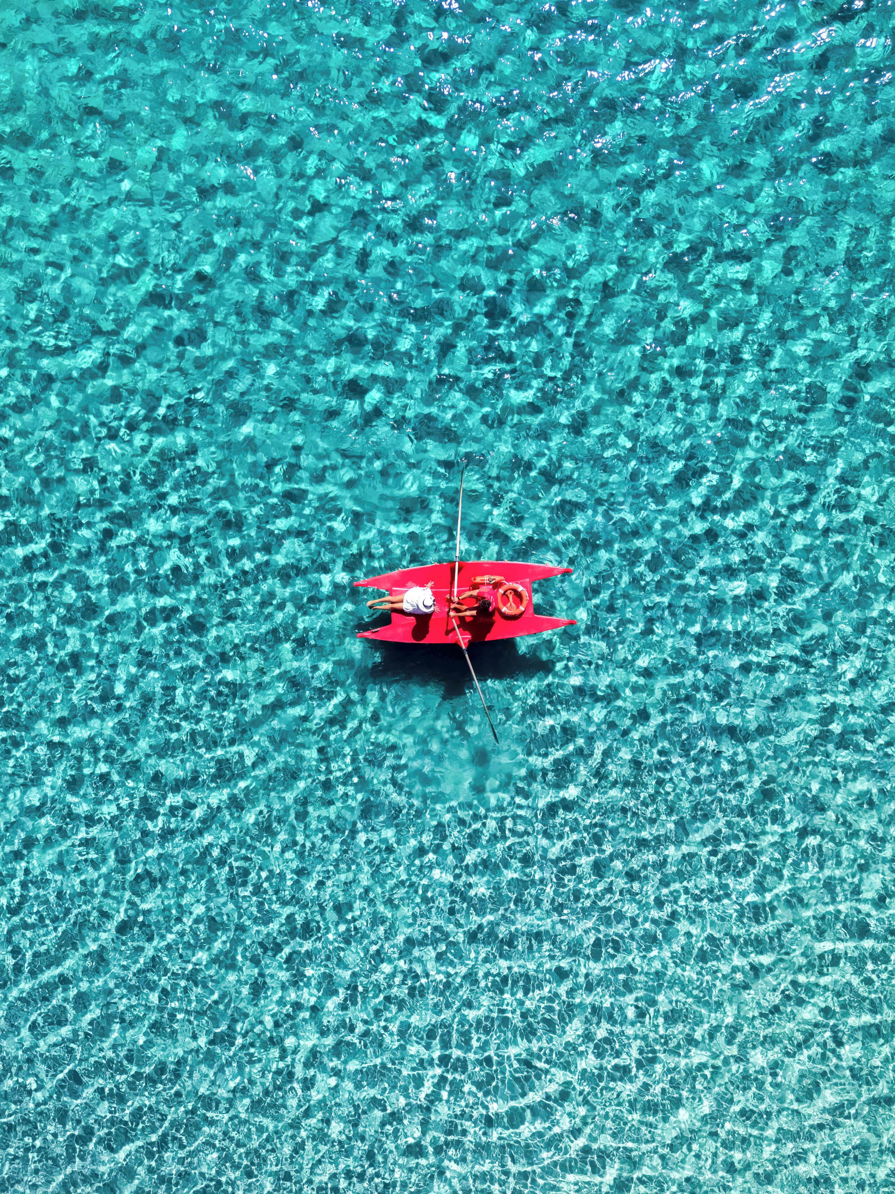 A red boat on clear turquoise water.