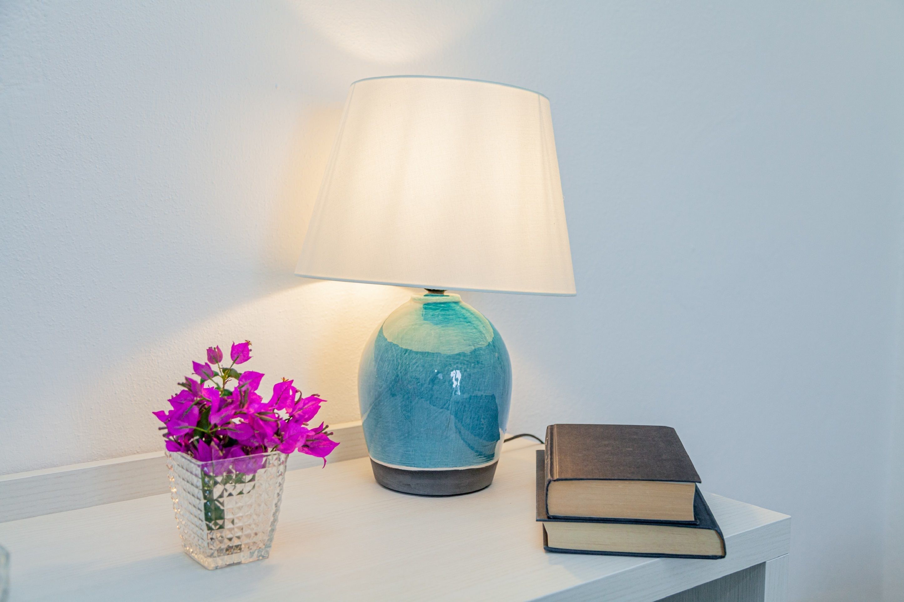 Un tavolo con una lampada, un vaso di fiori e un libro.