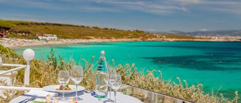 A table set for dining with a view of a beach and turquoise waters.