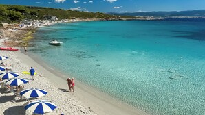Una playa con agua turquesa cristalina, arena blanca y sombrillas a rayas azules y blancas.