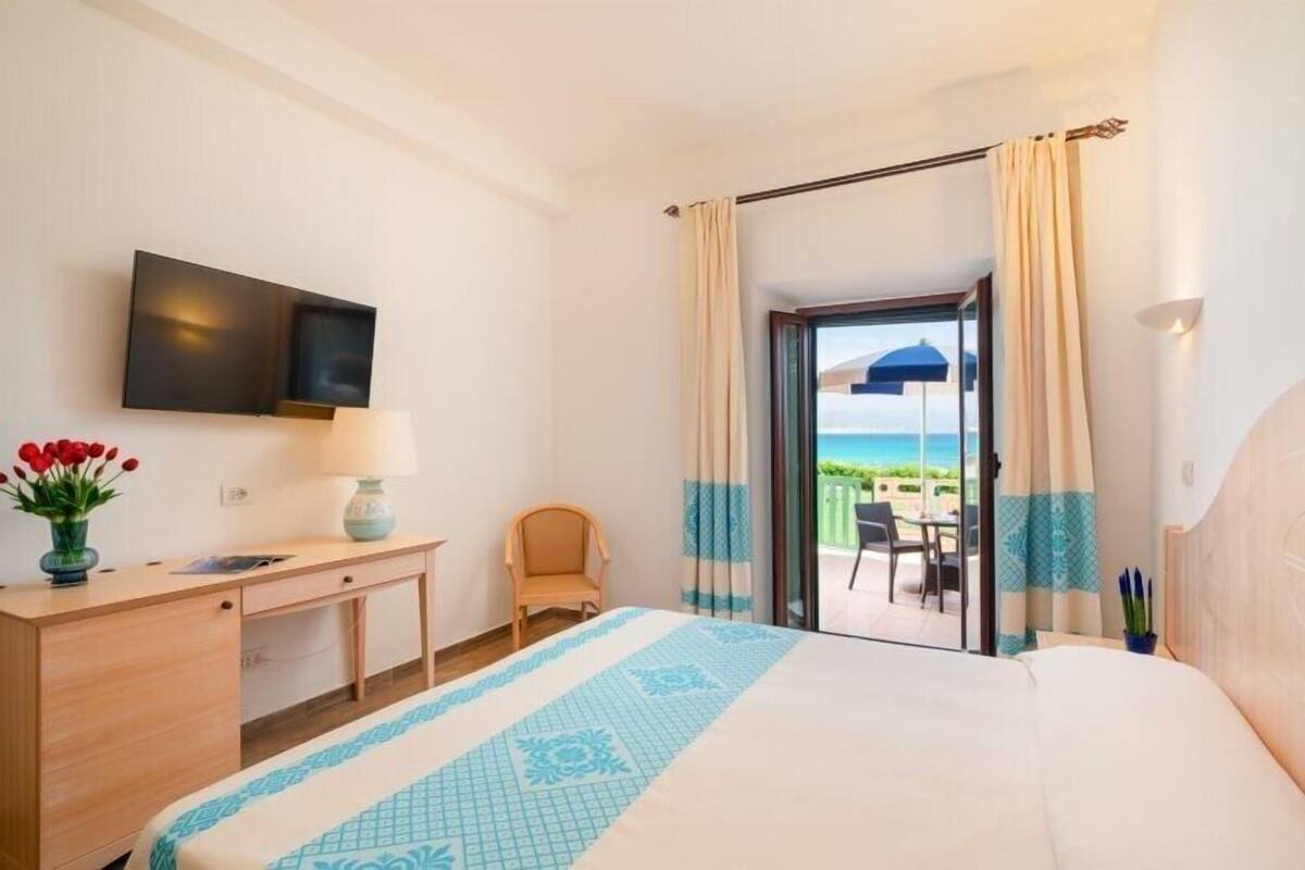 Ein Hotelzimmer mit Bett, Schreibtisch, Fernseher und Blick auf den Strand.