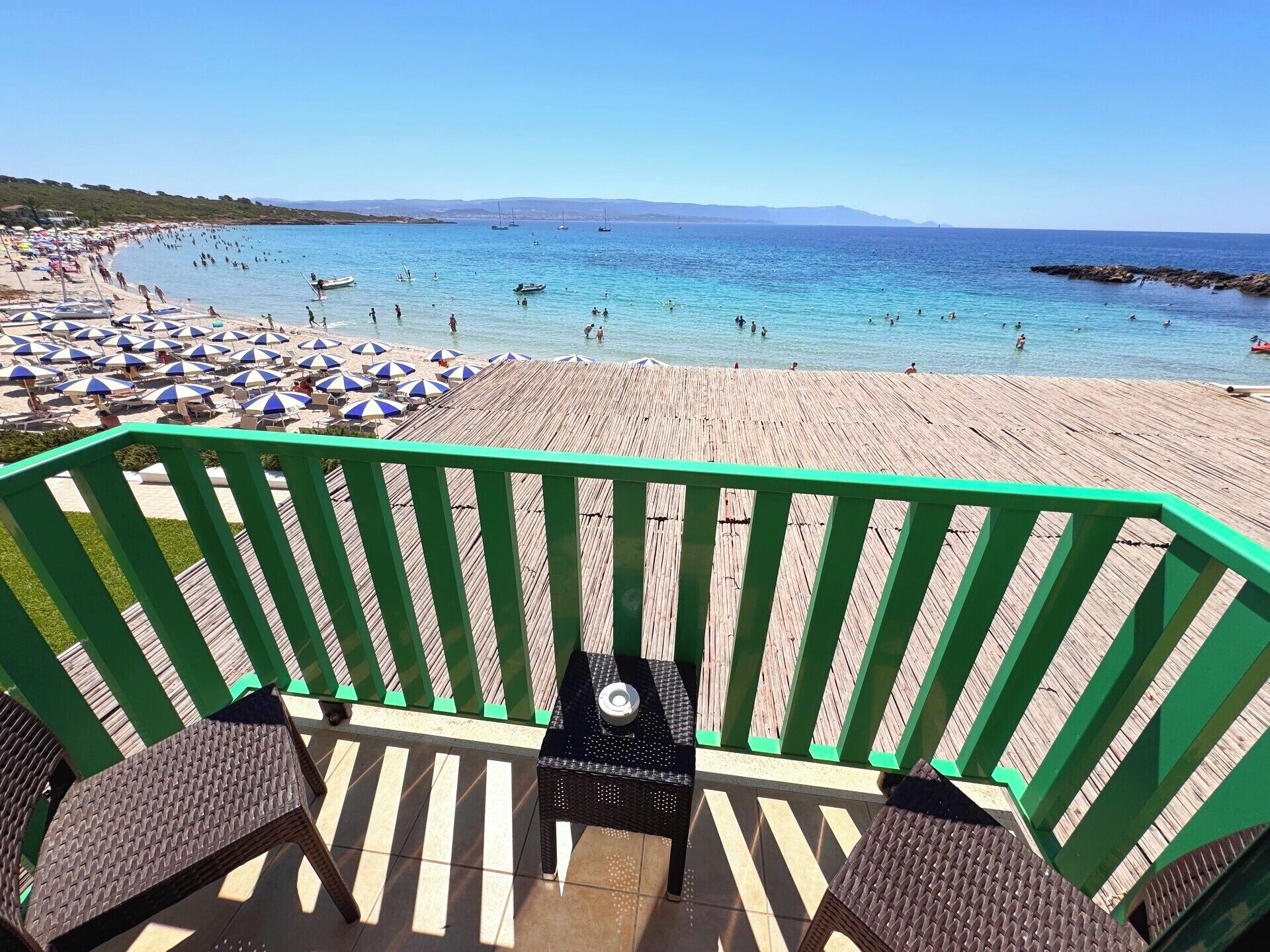 A beach with a wooden deck, wicker chairs, and umbrellas.