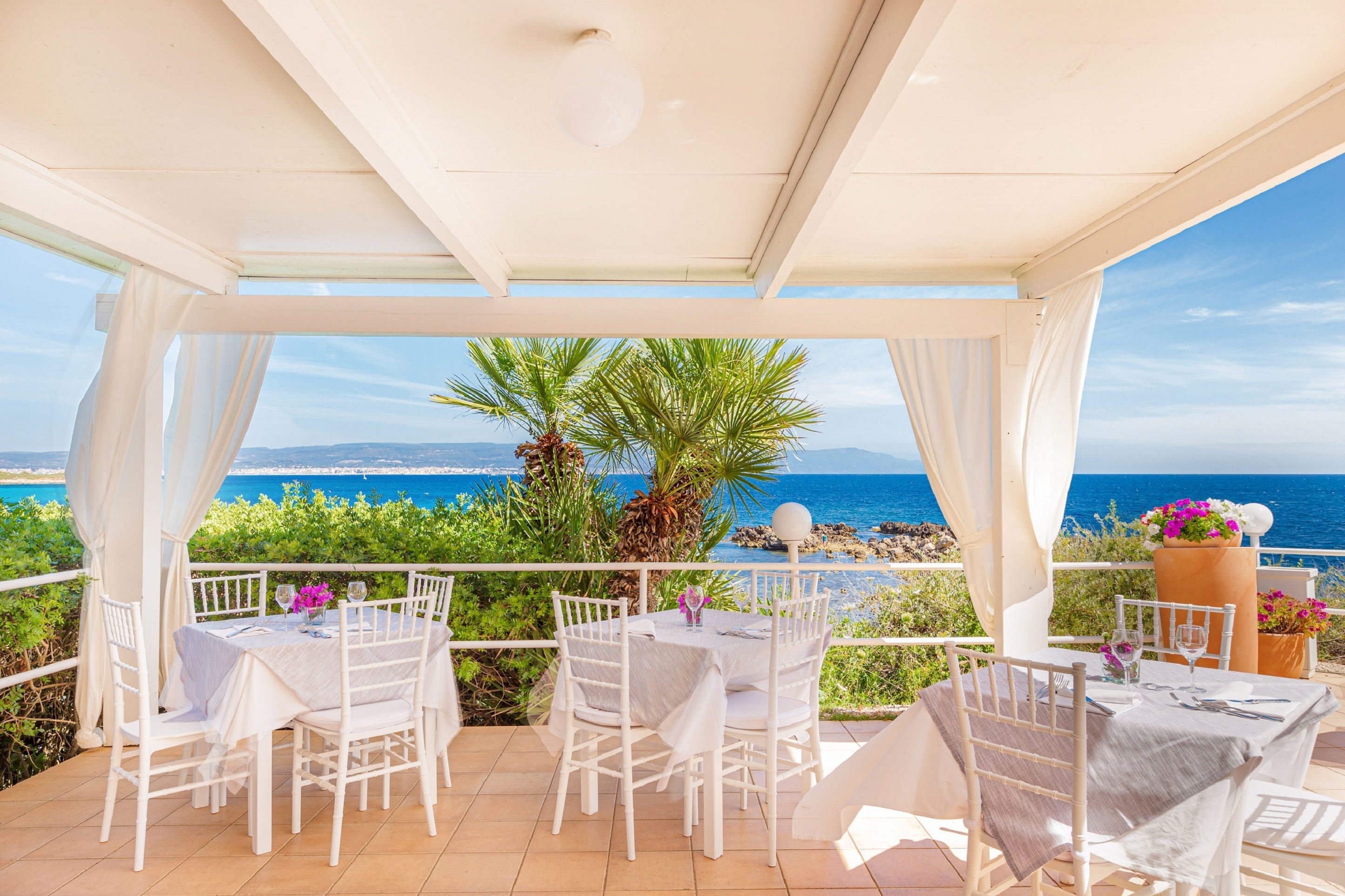 Un patio al aire libre con mobiliario blanco y vista al mar.