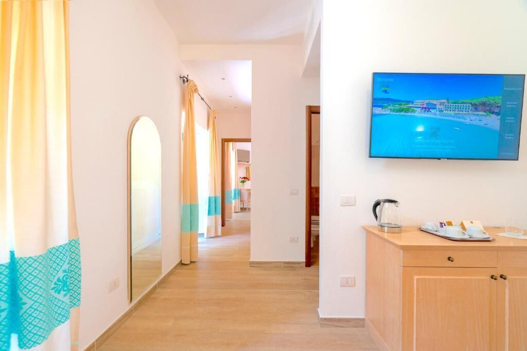 Un corridoio d'albergo con pavimento in legno, uno specchio, una televisione a parete e un mobiletto con bollitore e tazze.
