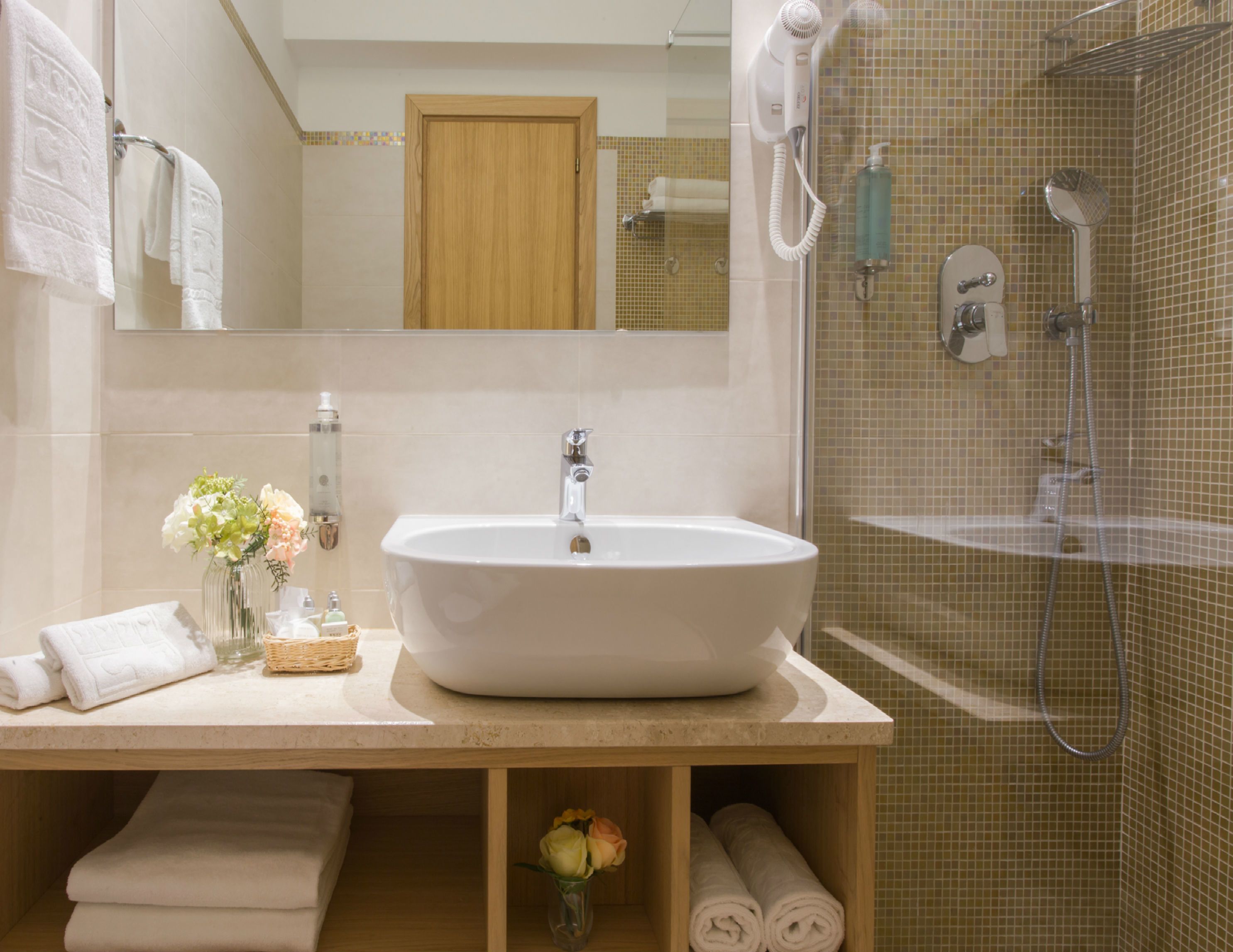 A bathroom with a large sink, a mirror, a shower area, and towels.
