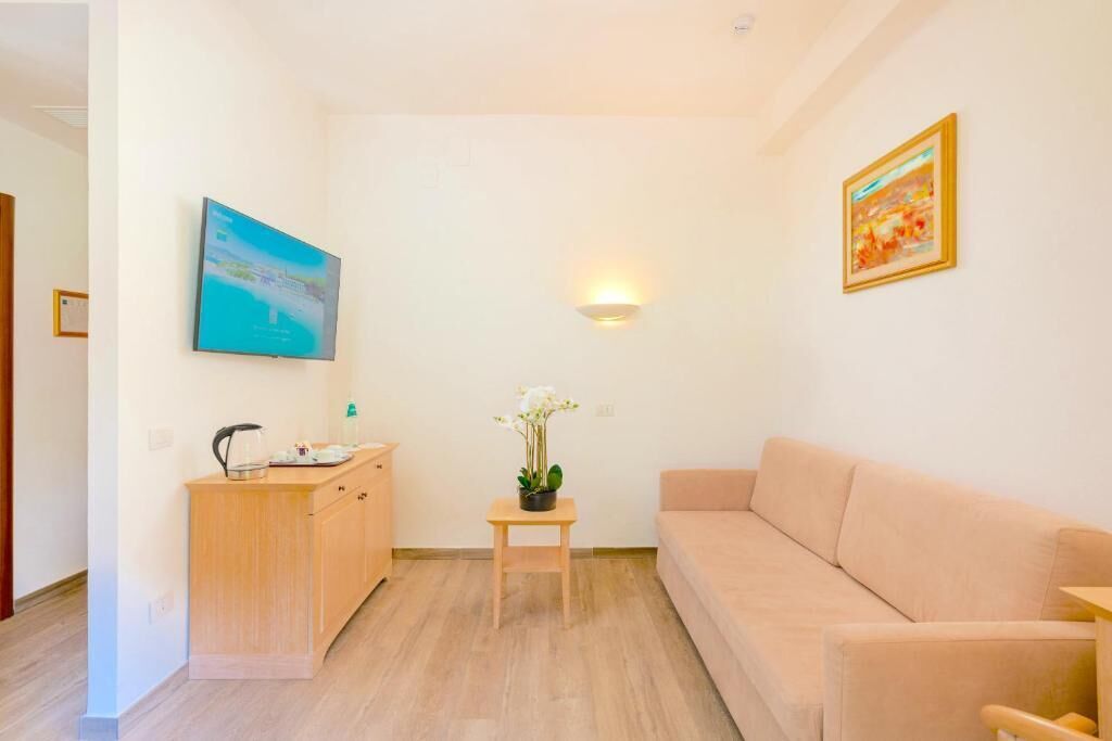 A room with a beige sofa, a wooden cabinet, a small table with a potted plant, a wall-mounted TV, and a wall-mounted light fixture.