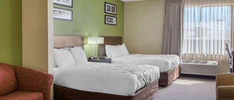 A hotel room with two beds, a red armchair, a bedside table with a lamp, and framed pictures on the wall.