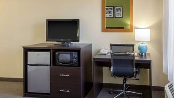 Een compacte hotelkamer met kitchenette, inclusief een koelkast, magnetron en een flatscreen televisie. Er is een bureau met een stoel en een lamp, en een spiegel aan de muur.