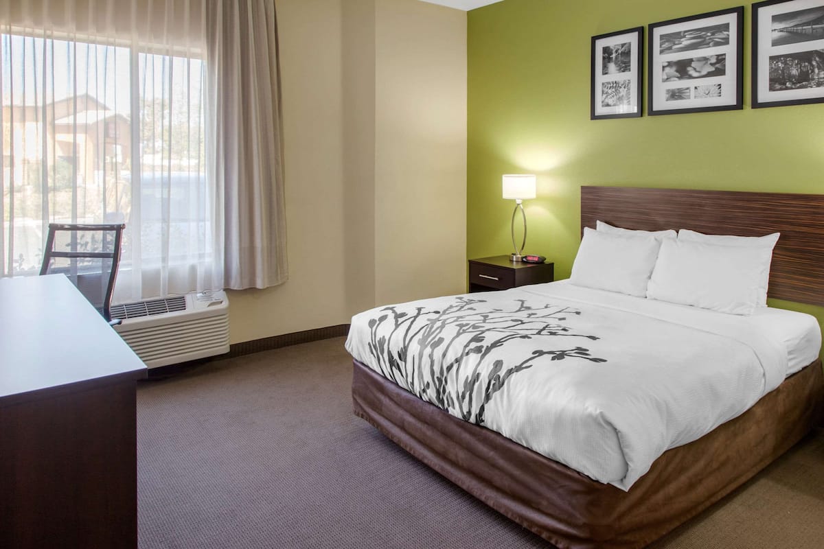 Habitación de hotel con cama, escritorio, silla, lámpara y ventana con cortinas.