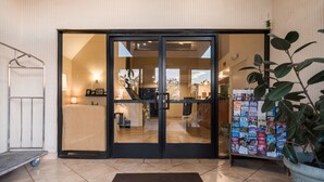 A hotel entrance with a sliding glass door, a welcome mat, a reception desk, and a plant. - Sleep Inn & Suites Bakersfield North (Bakersfield)