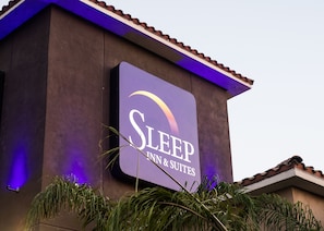 A Sleep Inn & Suites sign on a building with a purple-lit roof and a clear sky.