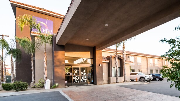 A hotel entrance with a covered walkway, palm trees, and parked cars. - Sleep Inn & Suites Bakersfield North (Bakersfield)