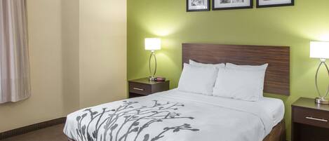 Habitación de hotel con cama, dos mesitas de noche y pared verde decorada con cuadros.