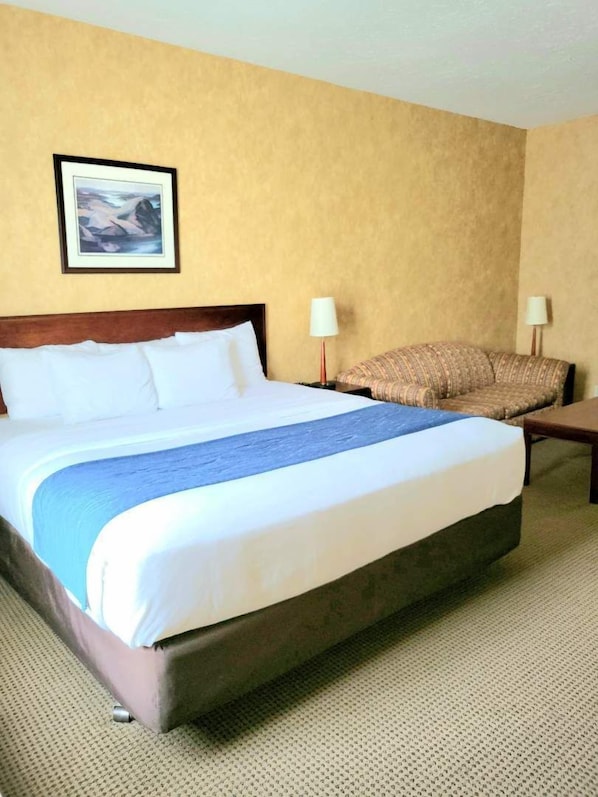 Una habitación de hotel con una cama grande, un sofá, dos lámparas y un cuadro en la pared.