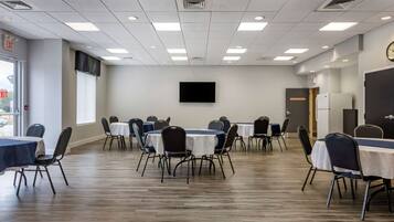 A conference room with multiple tables and chairs, a flat-screen TV mounted on the wall, and an exit sign.