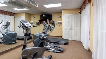 Un gimnasio con bicicletas estáticas, cintas de correr y un espejo grande.