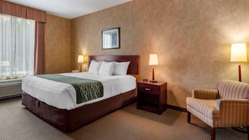 Habitación de hotel con una cama grande, dos mesitas de noche con lámparas, una silla y una ventana con cortinas.