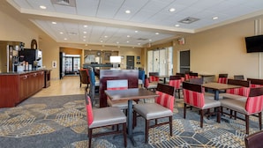 A hotel dining area with booths and tables, a coffee machine, and a refrigerator in the background.