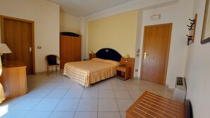 Una habitación de hotel con cama, escritorio, silla, armario y radiador.