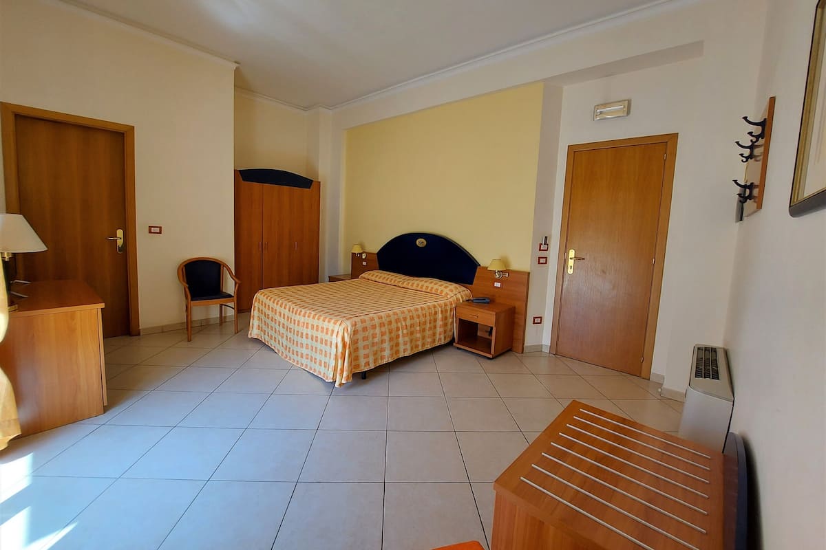 A hotel room with a bed, a desk, a chair, a wardrobe, and a radiator.