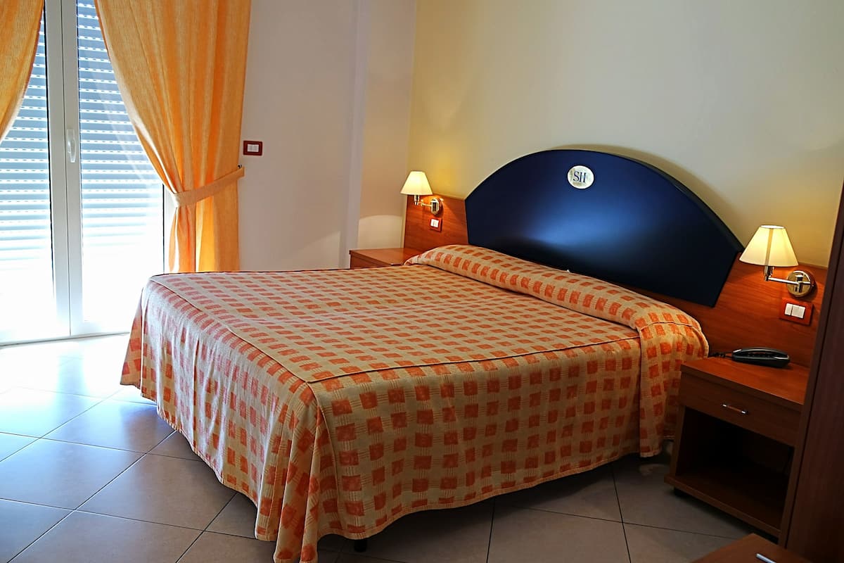 A hotel room with a bed, two bedside lamps, a nightstand, and a window with curtains.