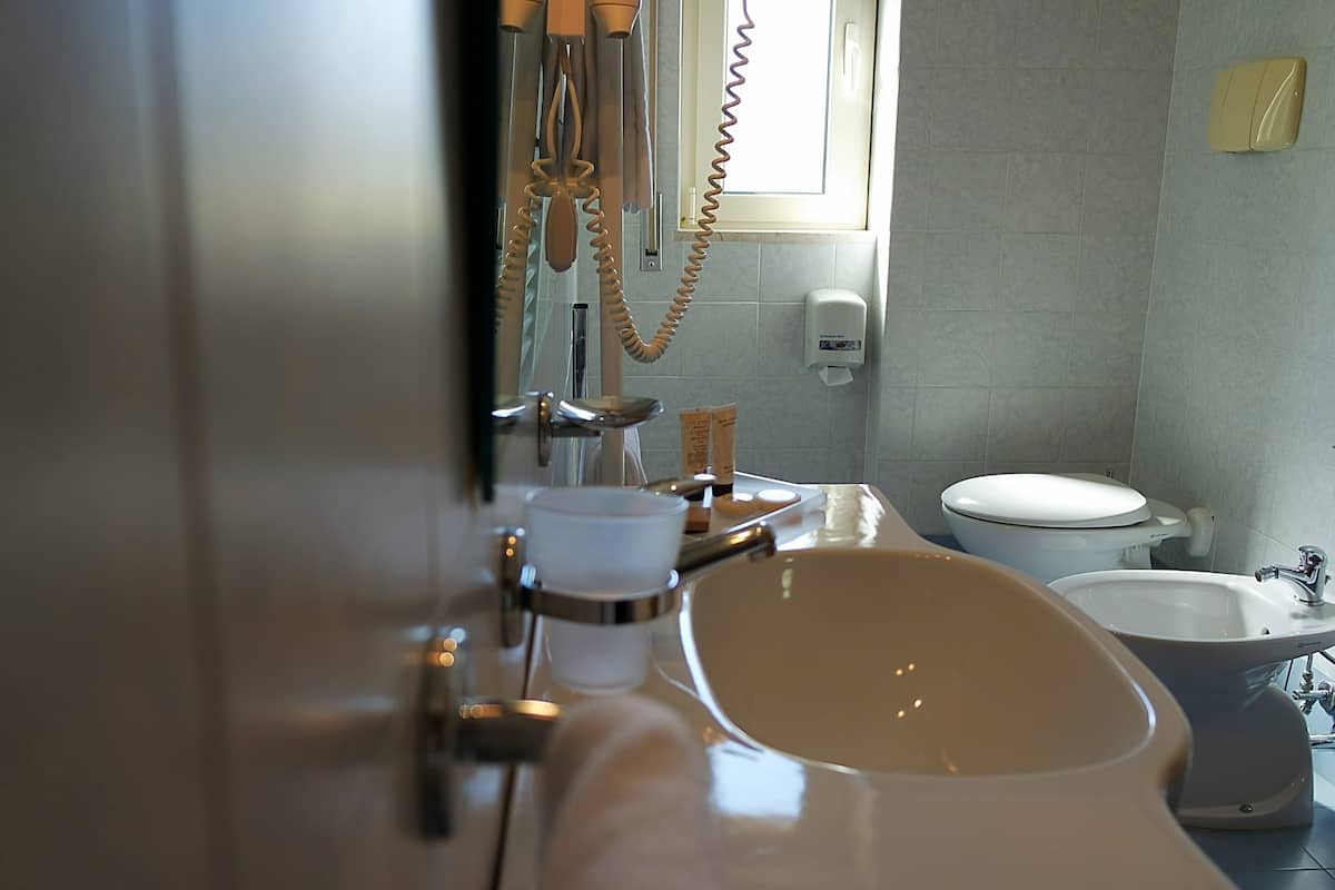 A bathroom with a bathtub, a sink, and a toilet. There is a hand soap dispenser on the wall.