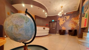 Un hall con un globo terráqueo sobre un pedestal, una recepción, un mapa del mundo en la pared y una escalera.